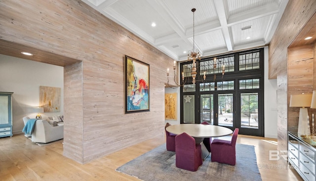 dining room featuring light wood-style flooring, a towering ceiling, wooden walls, coffered ceiling, and beamed ceiling