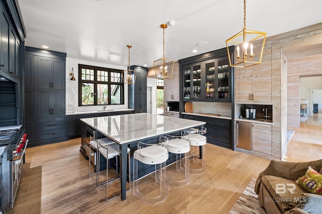 kitchen featuring light stone counters, hanging light fixtures, a center island, tasteful backsplash, and glass insert cabinets