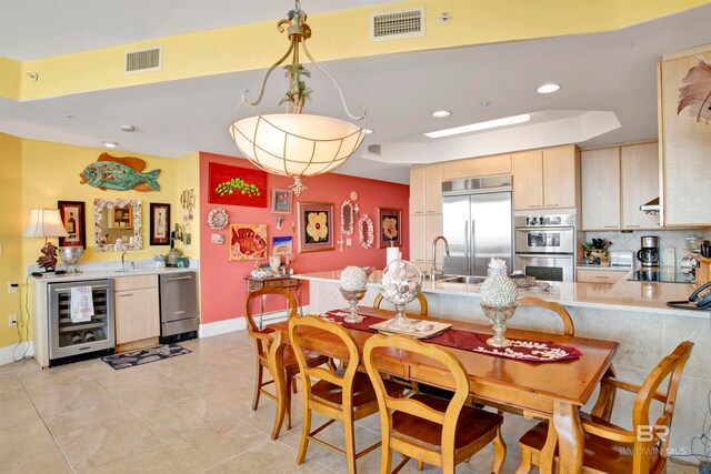 kitchen featuring light brown cabinetry, stainless steel appliances, pendant lighting, wine cooler, and light tile patterned floors