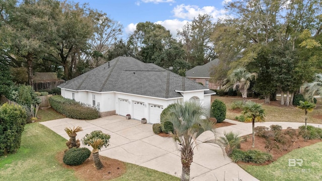 view of front of home featuring an attached garage, concrete driveway, roof with shingles, stucco siding, and a front lawn