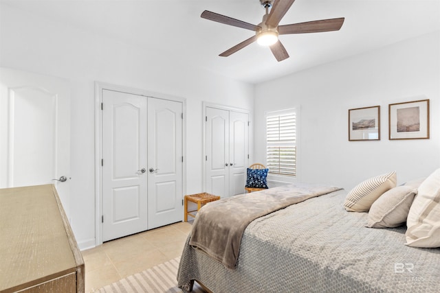 bedroom featuring light tile patterned floors, baseboards, a ceiling fan, and multiple closets