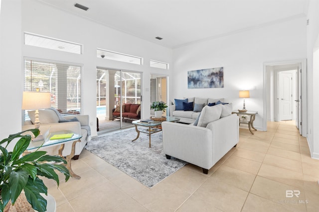 living area featuring a towering ceiling, visible vents, crown molding, and light tile patterned flooring