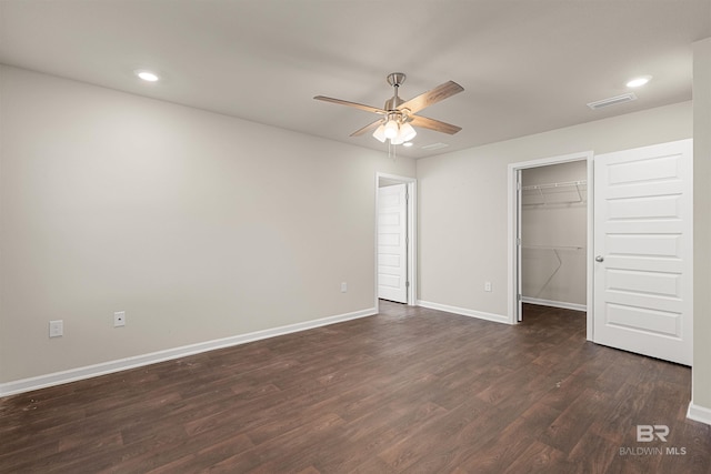 unfurnished bedroom featuring a walk in closet, ceiling fan, a closet, and dark wood-type flooring