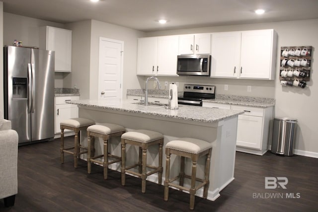 kitchen featuring appliances with stainless steel finishes, light stone counters, a center island with sink, white cabinets, and dark hardwood / wood-style floors