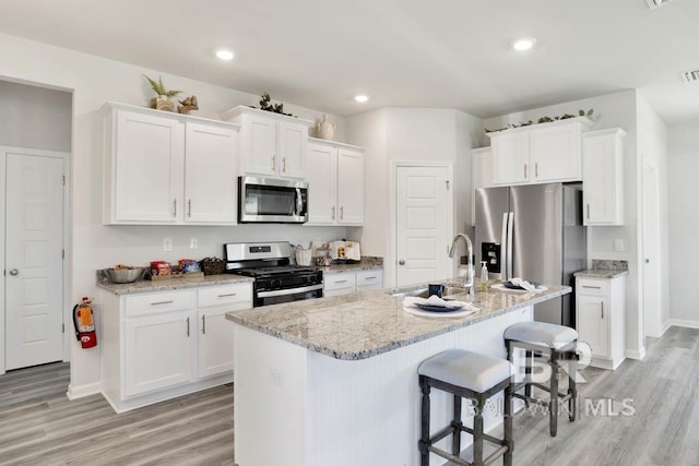 kitchen featuring white cabinets, appliances with stainless steel finishes, a center island with sink, and light hardwood / wood-style flooring