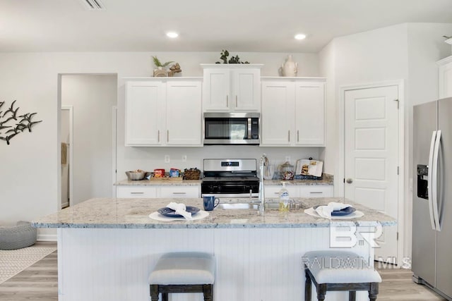 kitchen featuring a kitchen island with sink, white cabinets, light wood-type flooring, and appliances with stainless steel finishes