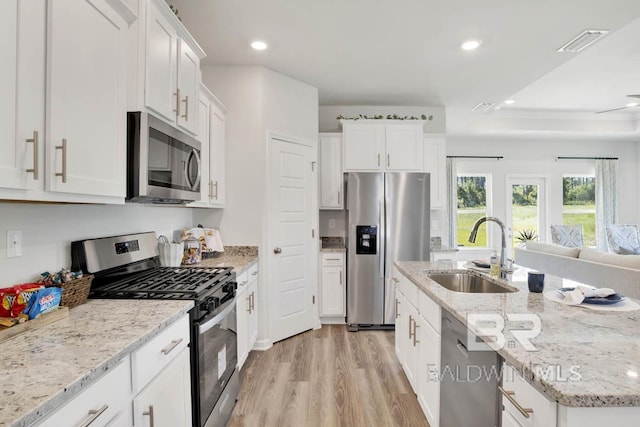 kitchen with appliances with stainless steel finishes, light stone counters, sink, white cabinets, and light hardwood / wood-style floors