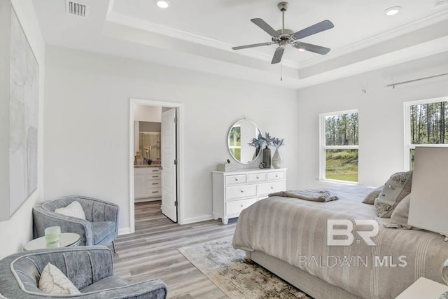 bedroom with a raised ceiling, crown molding, light hardwood / wood-style flooring, ceiling fan, and connected bathroom