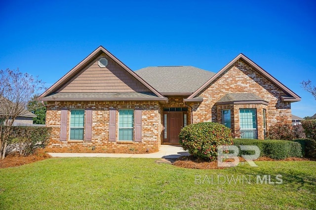 view of front of home featuring a shingled roof, a front lawn, and brick siding