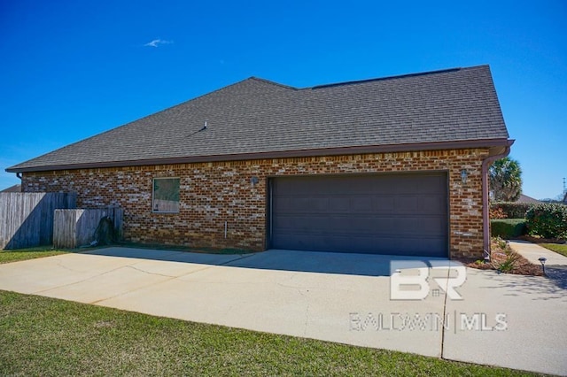 view of side of home featuring an attached garage, a shingled roof, concrete driveway, and brick siding