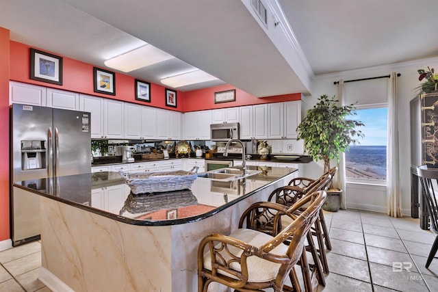 kitchen featuring appliances with stainless steel finishes, a sink, light tile patterned floors, baseboards, and ornamental molding