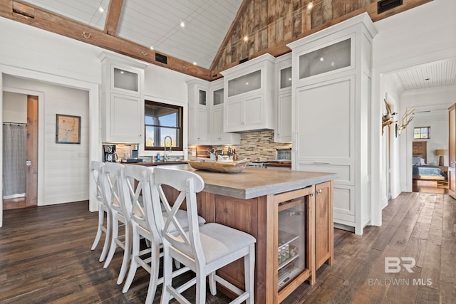 kitchen with a kitchen island, white cabinetry, dark hardwood / wood-style flooring, wine cooler, and high vaulted ceiling