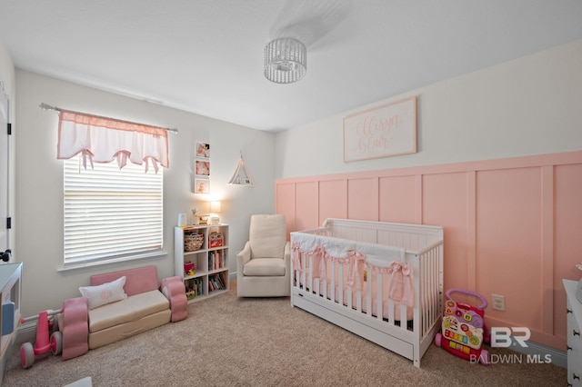 carpeted bedroom featuring a crib and a wainscoted wall