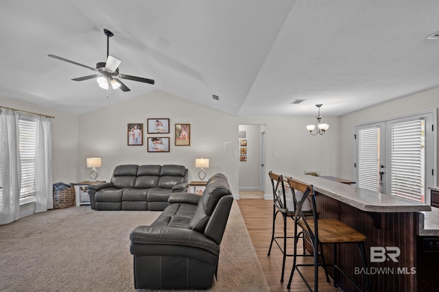 living area featuring vaulted ceiling, a bar, visible vents, and ceiling fan with notable chandelier