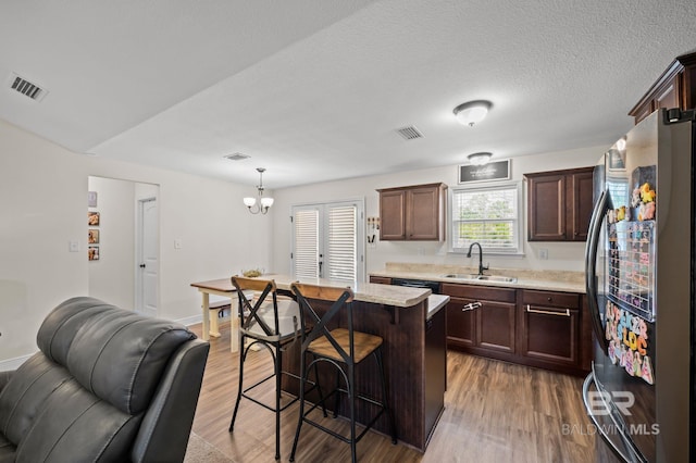 kitchen featuring freestanding refrigerator, wood finished floors, visible vents, and a sink