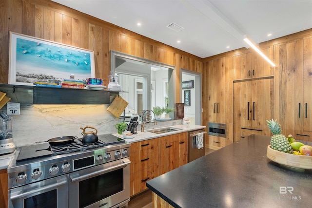 kitchen with appliances with stainless steel finishes, sink, hardwood / wood-style flooring, and wooden walls