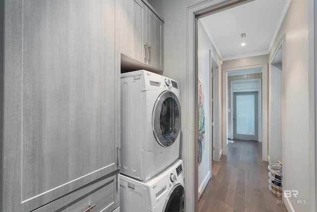 clothes washing area with cabinets, dark wood-type flooring, and stacked washer / drying machine