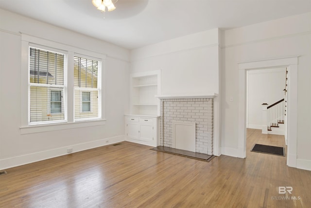 unfurnished living room featuring ceiling fan, built in features, a brick fireplace, and light hardwood / wood-style flooring