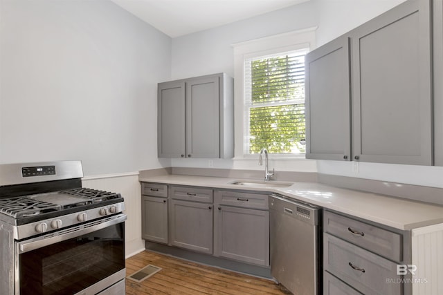 kitchen with stainless steel appliances, sink, gray cabinetry, and light hardwood / wood-style flooring