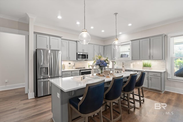 kitchen with a kitchen island with sink, dark wood-type flooring, stainless steel appliances, pendant lighting, and tasteful backsplash