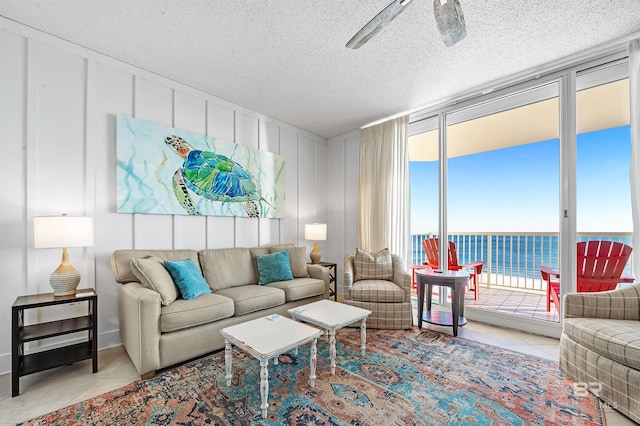 living room with expansive windows, a textured ceiling, ceiling fan, light tile patterned floors, and a water view