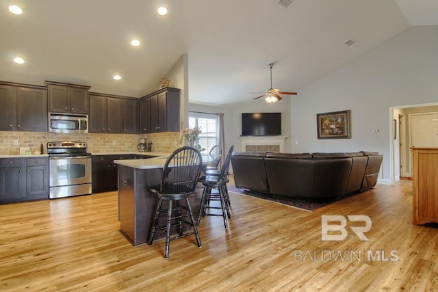 kitchen featuring dark brown cabinetry, a kitchen breakfast bar, stainless steel appliances, a tiled fireplace, and light hardwood / wood-style floors