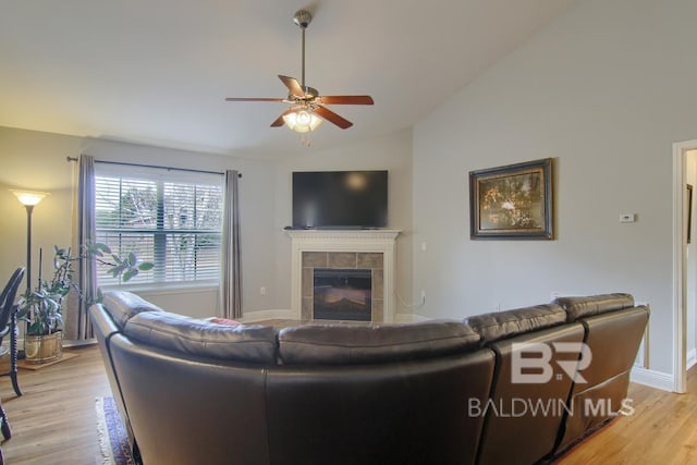 living room featuring lofted ceiling, a tile fireplace, light hardwood / wood-style floors, and ceiling fan