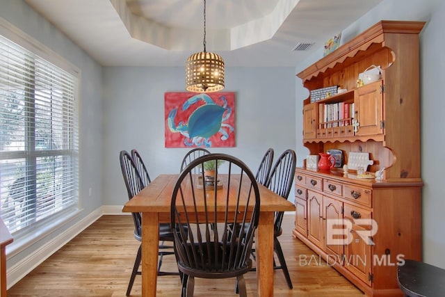 dining room with an inviting chandelier, a raised ceiling, and light wood-type flooring