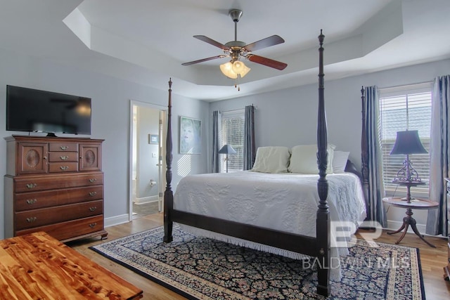 bedroom featuring ceiling fan, a tray ceiling, and light hardwood / wood-style floors