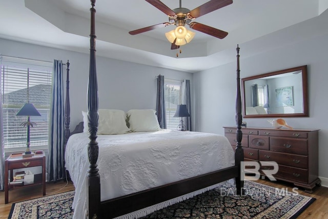 bedroom with a tray ceiling, wood-type flooring, and ceiling fan