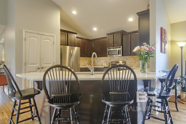 kitchen with vaulted ceiling, appliances with stainless steel finishes, tasteful backsplash, dark brown cabinetry, and light wood-type flooring