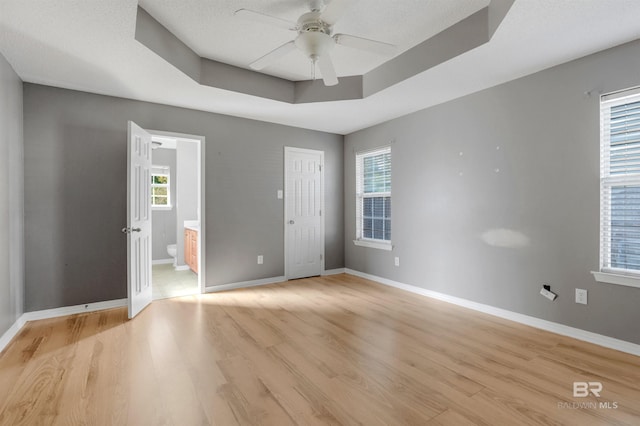 empty room with baseboards, a raised ceiling, light wood-style flooring, and a ceiling fan