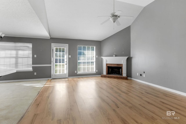 unfurnished living room featuring a ceiling fan, wood finished floors, baseboards, lofted ceiling, and a fireplace