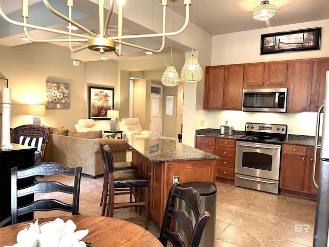 kitchen with a kitchen island, open floor plan, appliances with stainless steel finishes, brown cabinets, and dark stone countertops