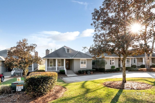 view of front facade featuring a front yard, a porch, a shingled roof, a chimney, and board and batten siding