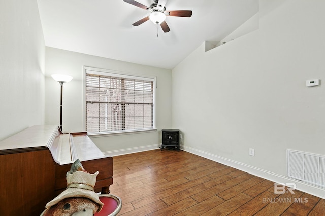 unfurnished room featuring lofted ceiling, hardwood / wood-style floors, ceiling fan, and a wood stove