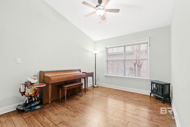 misc room featuring ceiling fan, vaulted ceiling, a wood stove, and light hardwood / wood-style floors