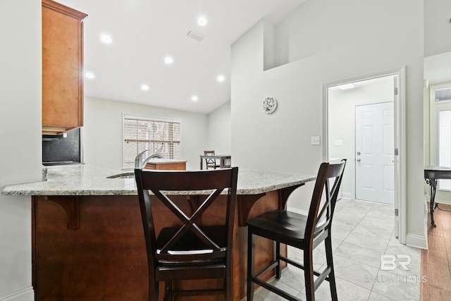 kitchen with light stone counters, sink, light tile patterned floors, and kitchen peninsula