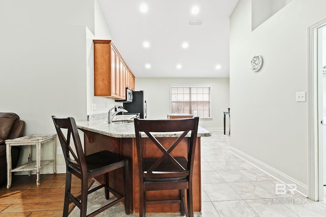 kitchen with light stone counters, sink, a breakfast bar area, and kitchen peninsula