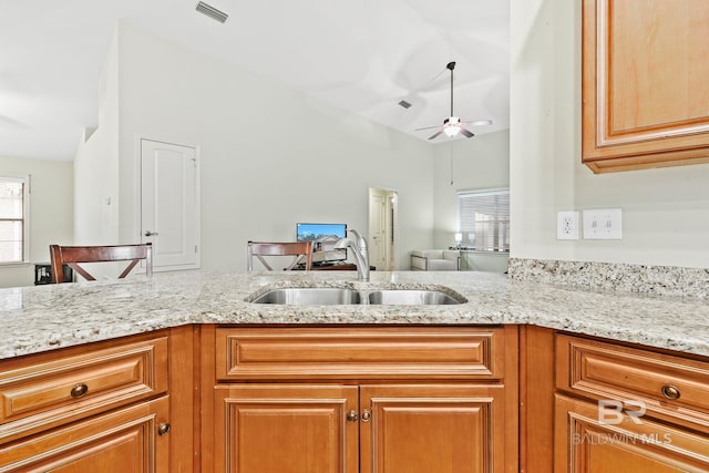 kitchen with lofted ceiling, kitchen peninsula, sink, and light stone countertops