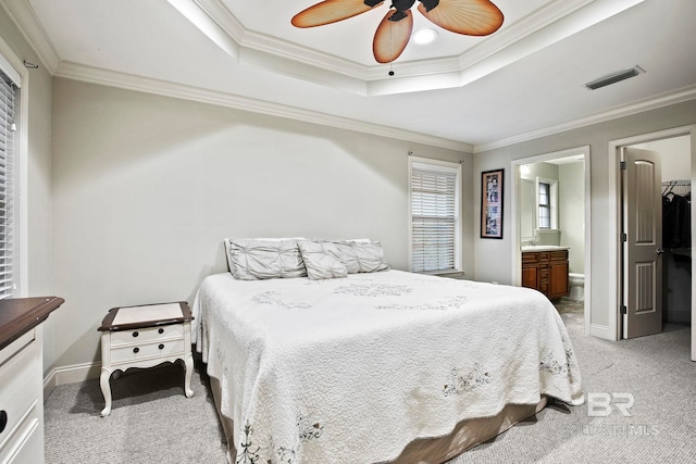 carpeted bedroom with ceiling fan, ensuite bathroom, a tray ceiling, and ornamental molding