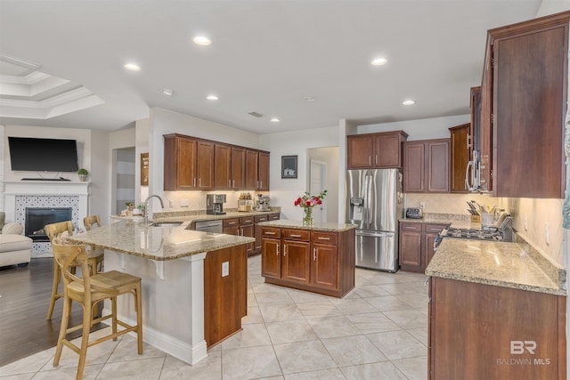 kitchen featuring a sink, open floor plan, stainless steel appliances, a peninsula, and light stone countertops