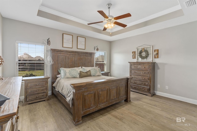 bedroom with multiple windows, a raised ceiling, and light wood-style floors