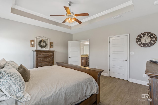 bedroom with wood finished floors, baseboards, visible vents, a tray ceiling, and crown molding