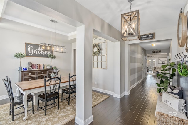 dining space with hardwood / wood-style floors, visible vents, baseboards, an inviting chandelier, and a raised ceiling