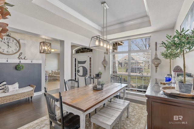 dining room with wood finished floors, an inviting chandelier, crown molding, a textured ceiling, and a raised ceiling