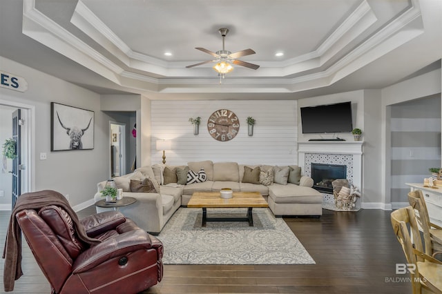 living room with baseboards, a raised ceiling, dark wood finished floors, and ornamental molding