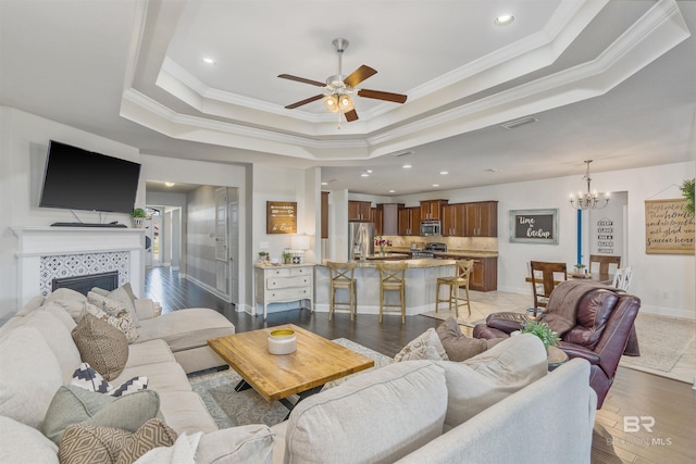 living room with baseboards, light wood-style flooring, crown molding, a tiled fireplace, and a raised ceiling