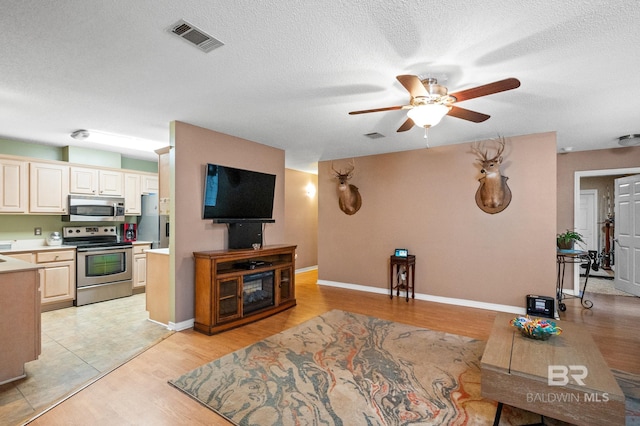 living room with ceiling fan, a textured ceiling, and light wood-type flooring