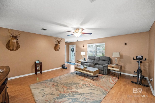 living room featuring hardwood / wood-style flooring, ceiling fan, and a textured ceiling